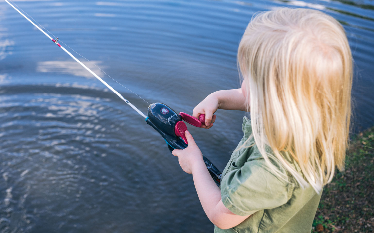 a girl fishing at the edge of a lake
