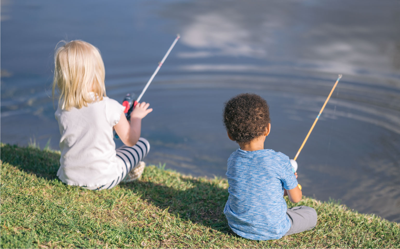a boy and girl fishing at the edge of a lake