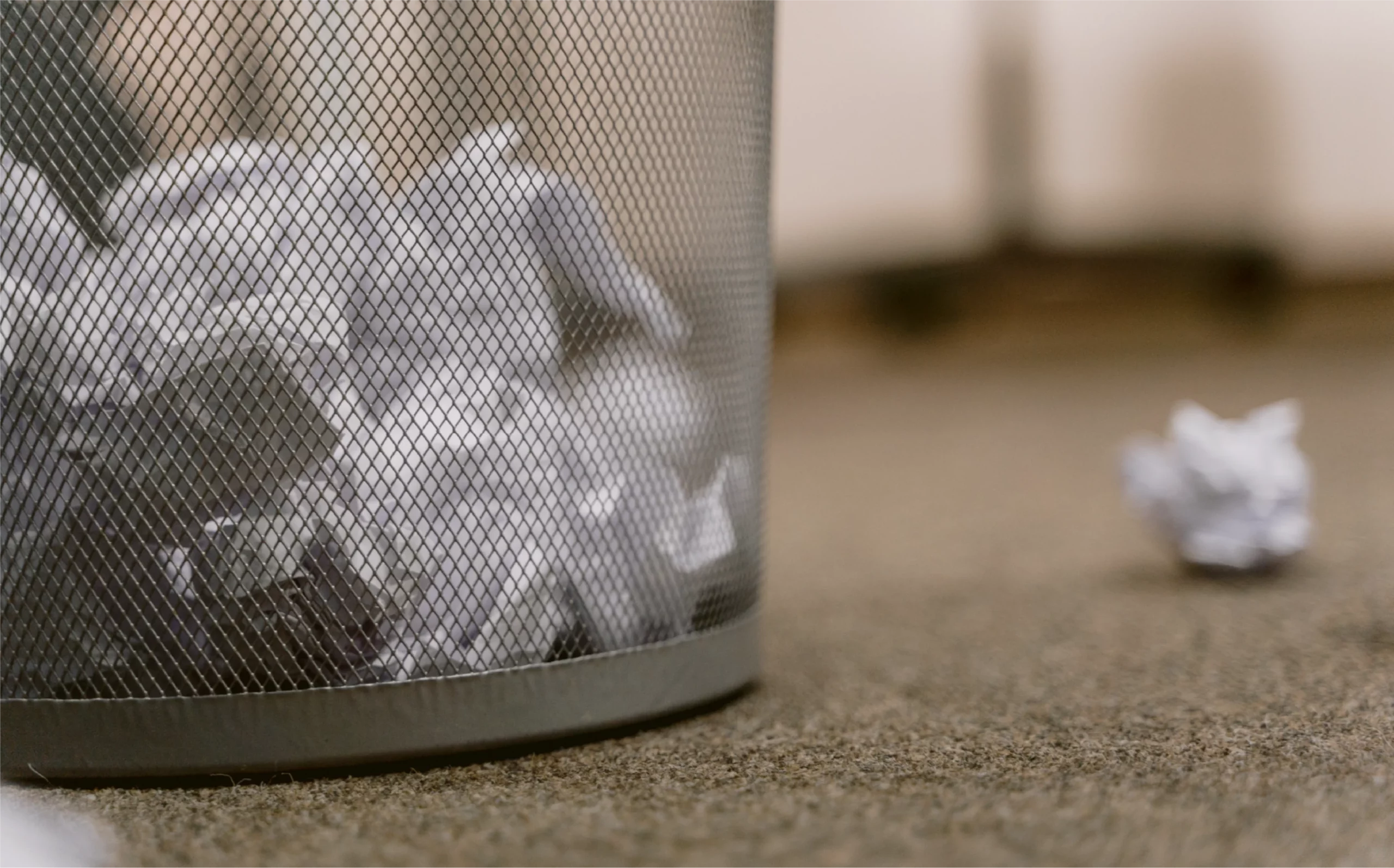 wire mesh wastebasket with crumpled paper inside it and beside it